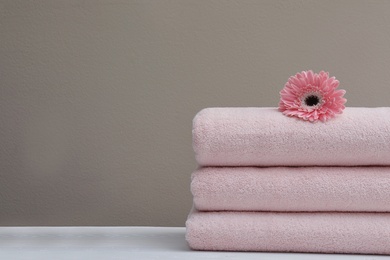 Photo of Stack of fresh towels with flower on table. Space for text