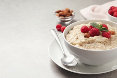 Tasty oatmeal porridge with raspberries and almond nuts served on light table, space for text