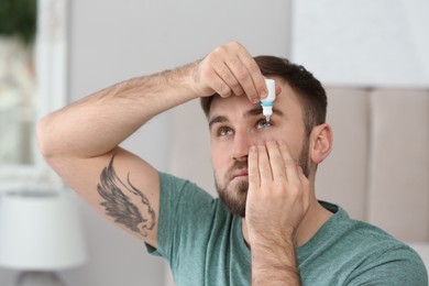 Young man using eye drops in room