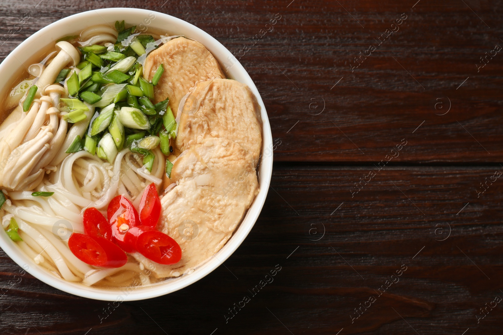 Photo of Delicious ramen with meat and mushrooms in bowl on wooden table, top view. Space for text