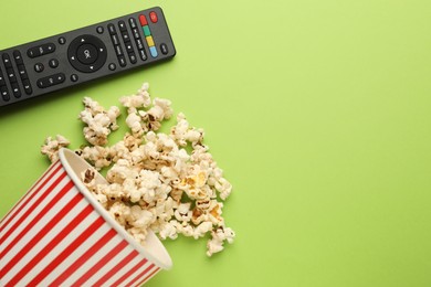 Remote control and cup of popcorn on light green background, flat lay. Space for text