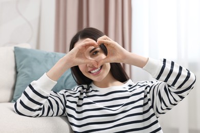 Photo of Happy young woman making heart with hands at home