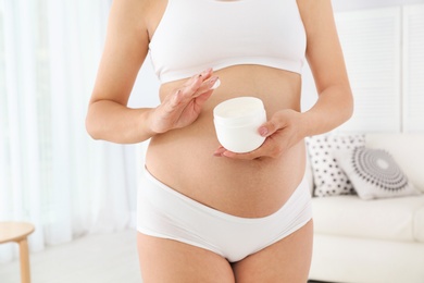 Photo of Pregnant woman holding body cream at home, closeup