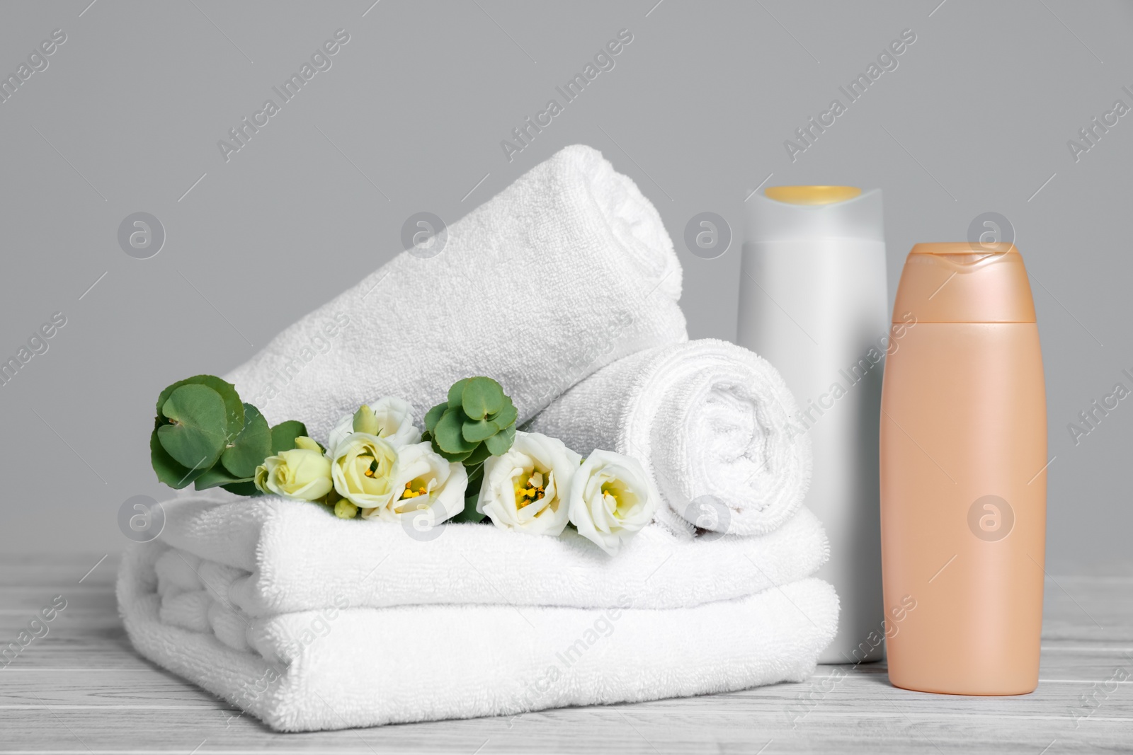 Photo of Soft white towels with flowers and cosmetic products on wooden table against grey background