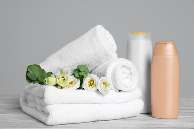 Photo of Soft white towels with flowers and cosmetic products on wooden table against grey background