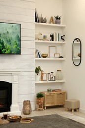 Photo of Shelves with different decor near decorative fireplace in living room. Cozy interior design