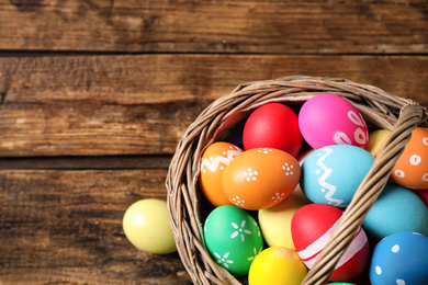 Photo of Colorful Easter eggs in basket on wooden background, top view. Space for text