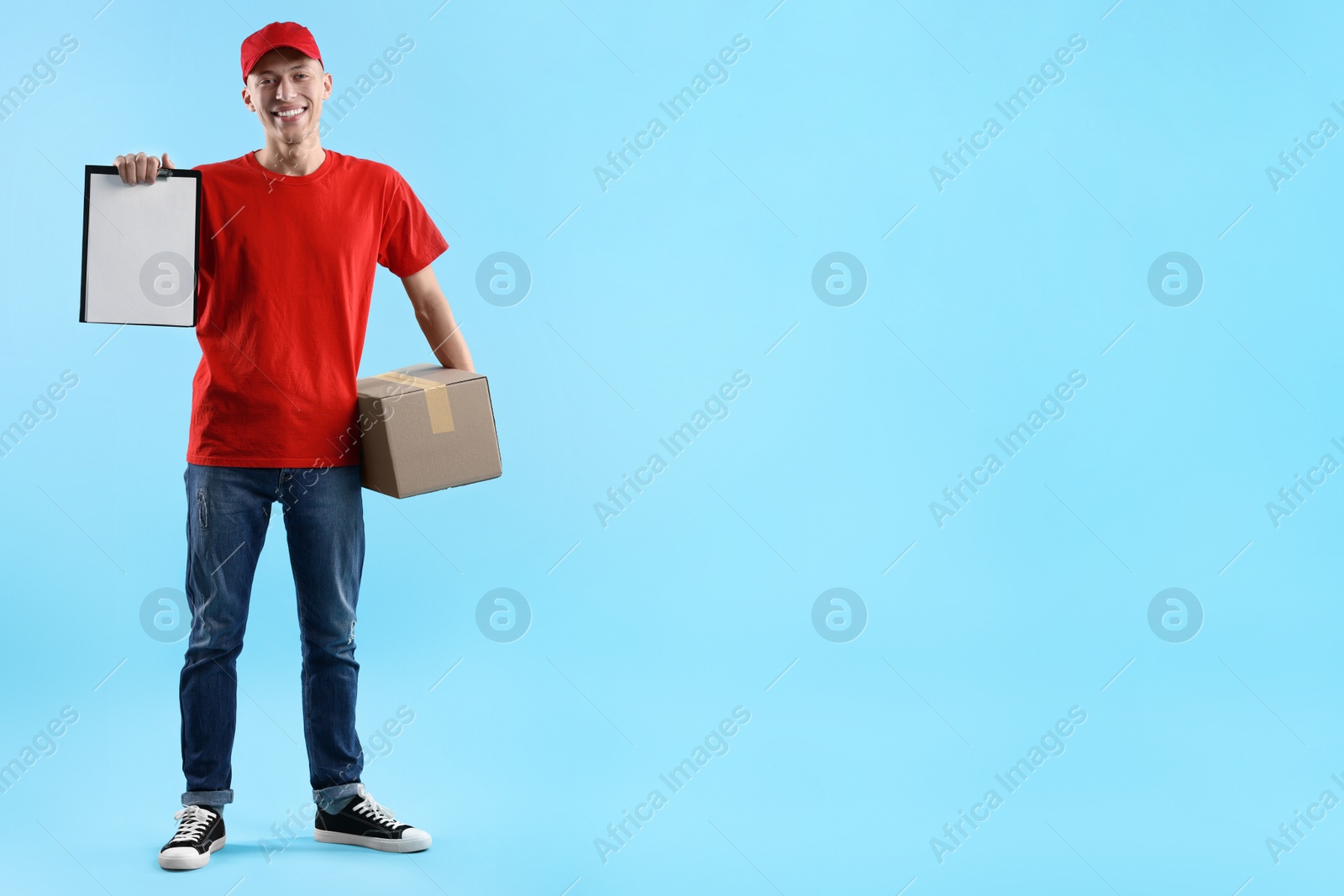 Photo of Happy courier with parcel and clipboard on light blue background. Space for text