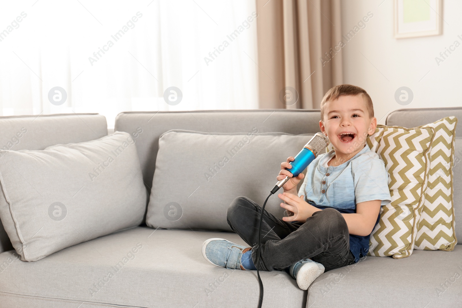 Photo of Cute funny boy with microphone sitting on sofa at home. Space for text