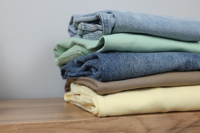 Photo of Stack of different folded clothes on wooden table near grey wall, closeup. Space for text