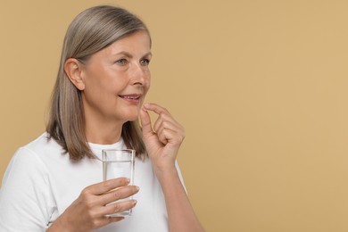 Photo of Senior woman with glass of water taking pill on beige background. Space for text