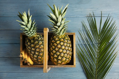 Photo of Fresh pineapples in box on wooden background, top view