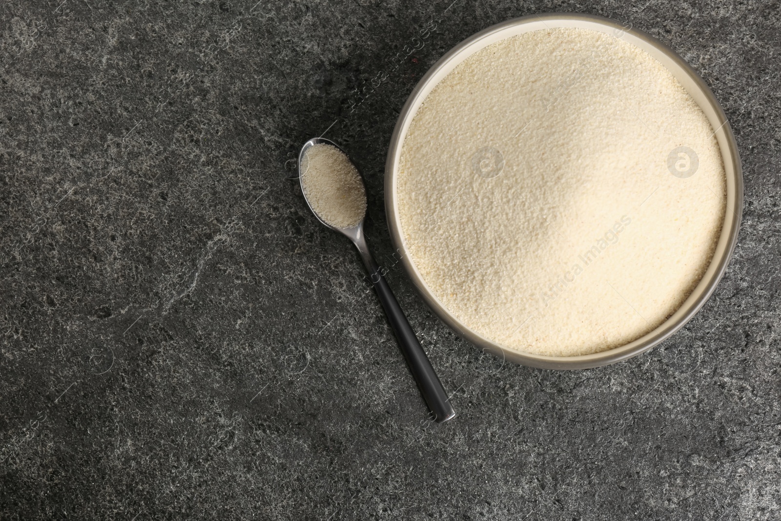 Photo of Semolina in bowl and spoon on grey table, flat lay. Space for text