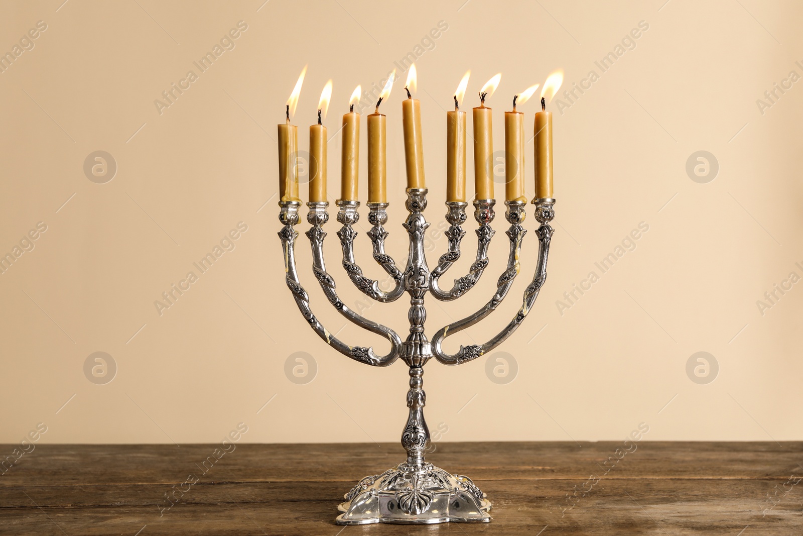 Photo of Silver menorah with candles on wooden table against beige background. Hanukkah celebration