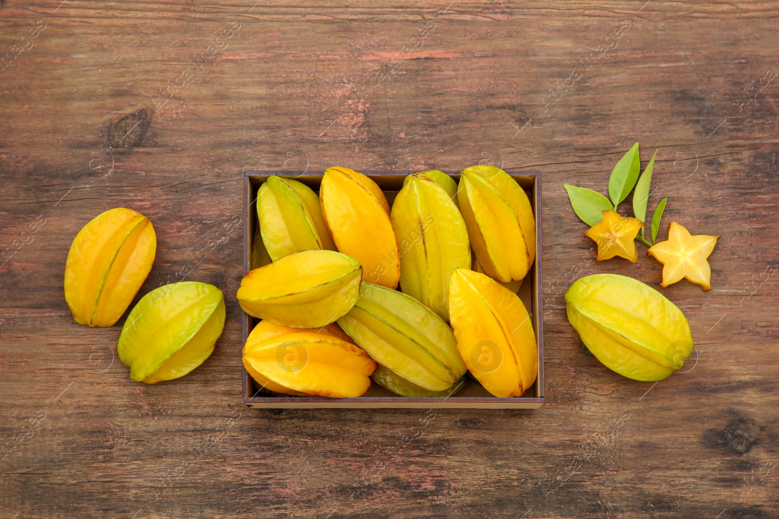 Photo of Cut and whole delicious ripe carambolas with leaves on wooden table, flat lay