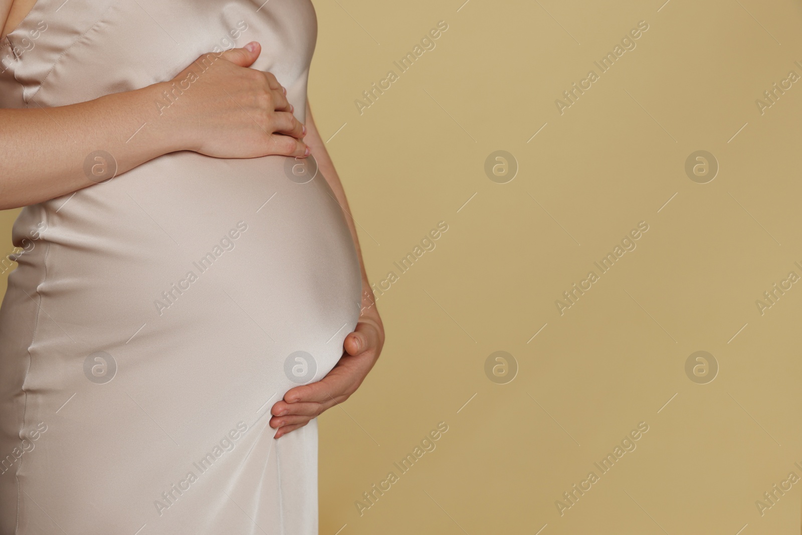 Photo of Pregnant woman touching belly on beige background, closeup. Space for text