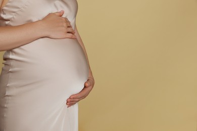 Photo of Pregnant woman touching belly on beige background, closeup. Space for text