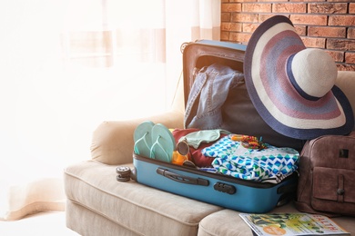 Photo of Open suitcase with different clothes and accessories on sofa indoors. Packing for vacation