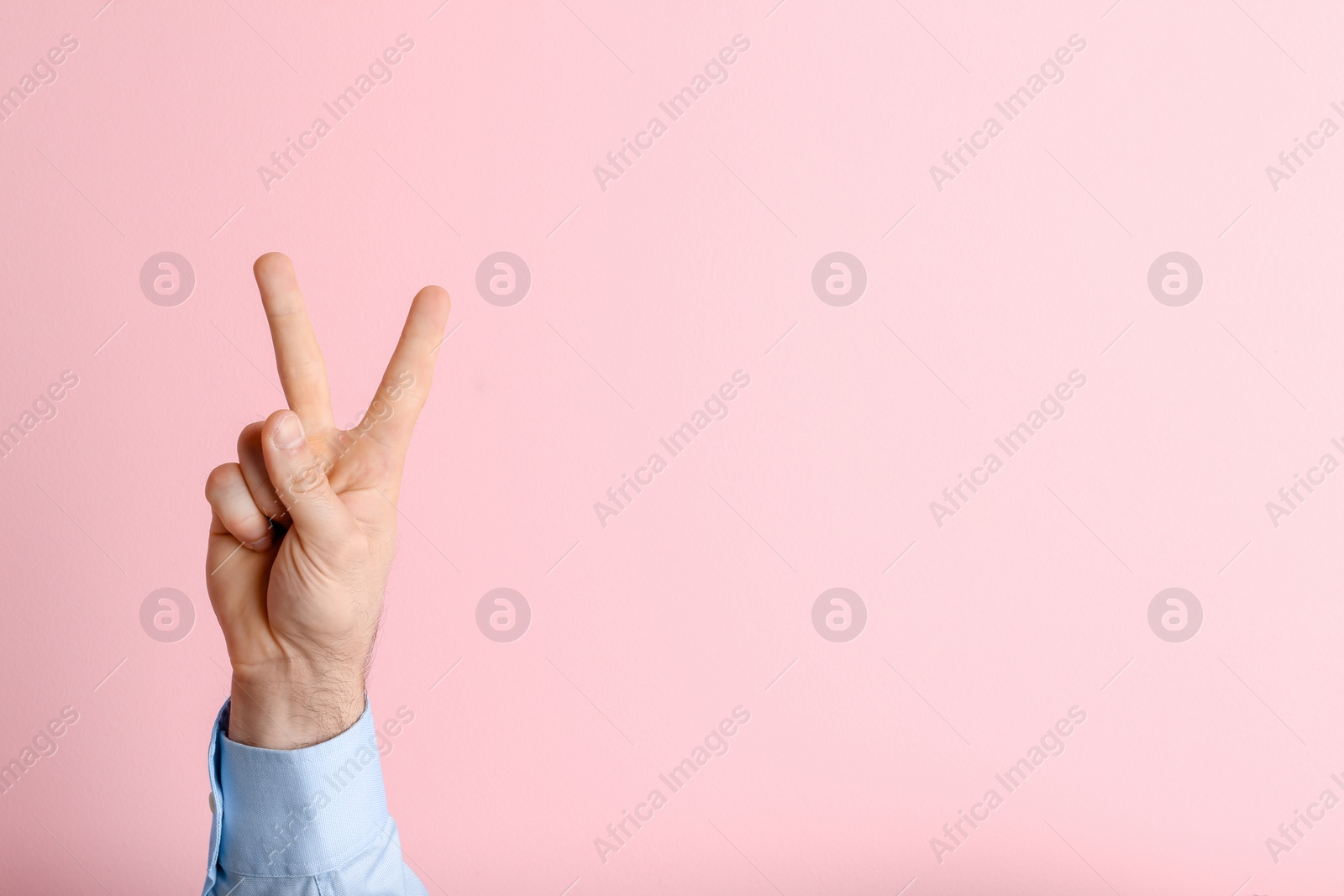 Photo of Young man showing victory gesture on color background. Space for text