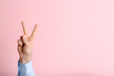 Photo of Young man showing victory gesture on color background. Space for text