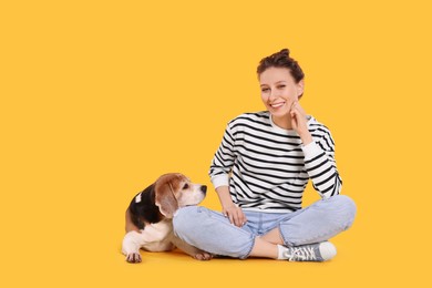 Photo of Happy young woman with cute Beagle dog on orange background. Lovely pet