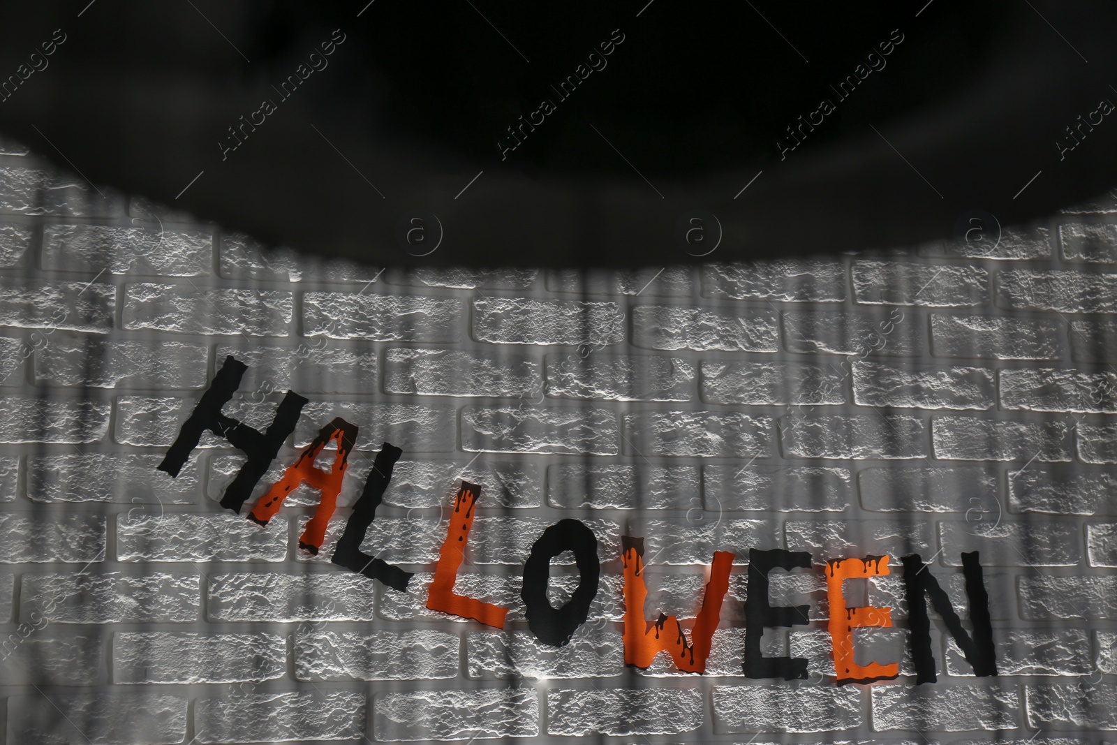 Photo of Word Halloween made of colorful letters and festive decor on brick wall