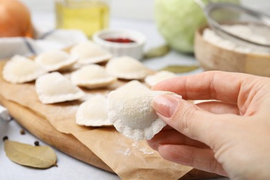 Photo of Woman holding raw dumpling (varenyk) with tasty filling at table, closeup