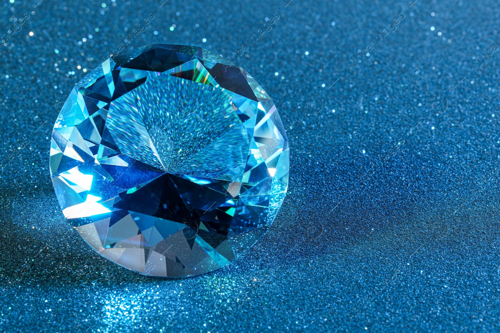 Photo of Beautiful dazzling diamond on light blue glitter background, closeup. Space for text