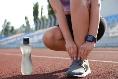 Photo of Woman with fitness tracker tying shoelaces at stadium, closeup