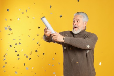 Photo of Man blowing up party popper on yellow background