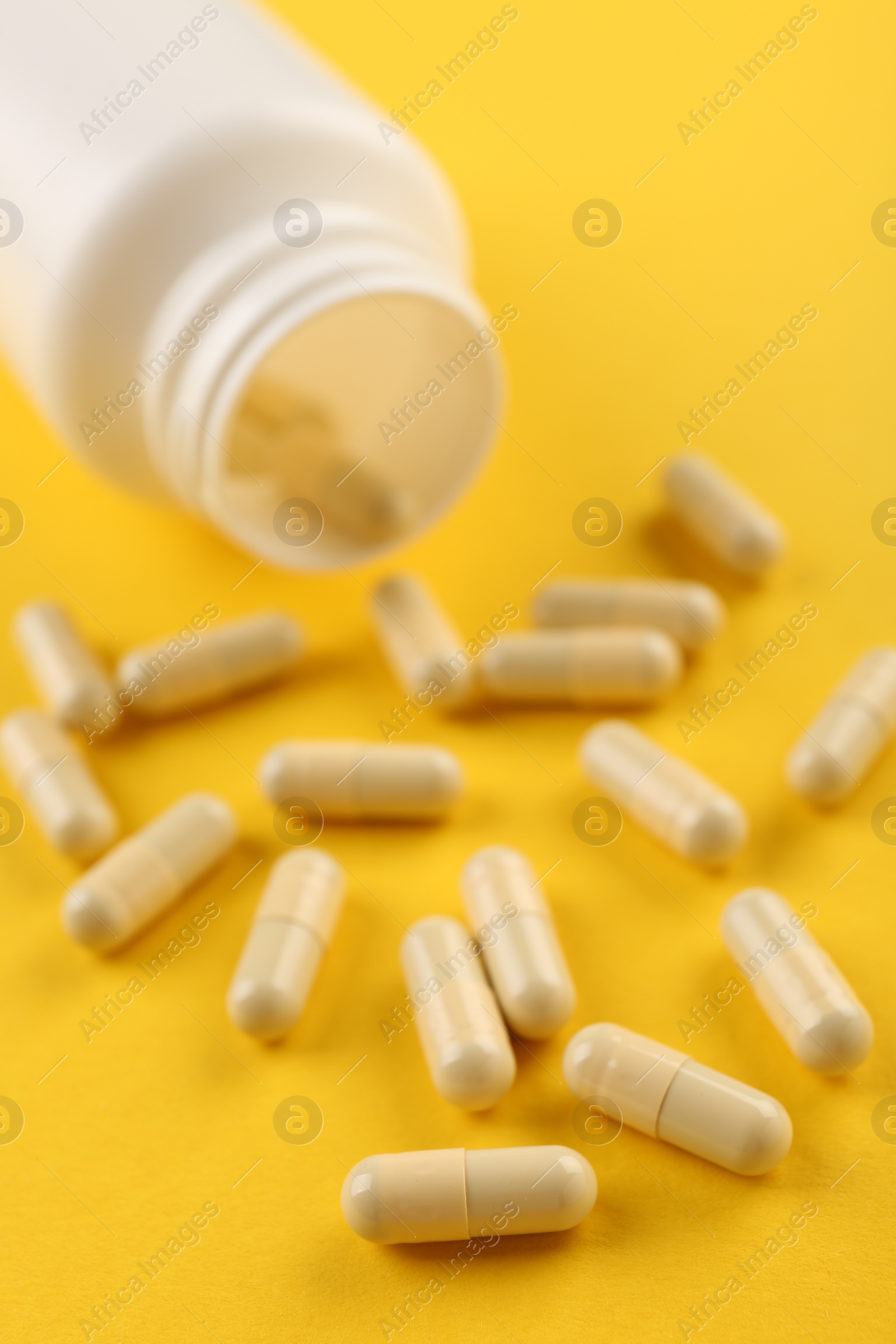 Photo of Bottle and vitamin capsules on yellow background, closeup