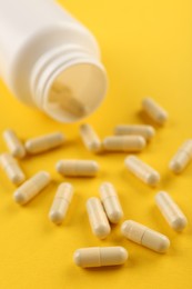 Photo of Bottle and vitamin capsules on yellow background, closeup