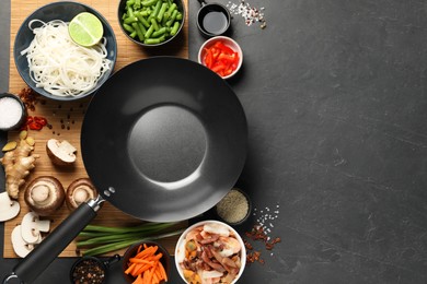 Flat lay composition with black wok, spices and products on dark textured table. Space for text