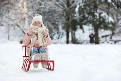 Cute little girl enjoying sledge ride through snow in winter park, space for text