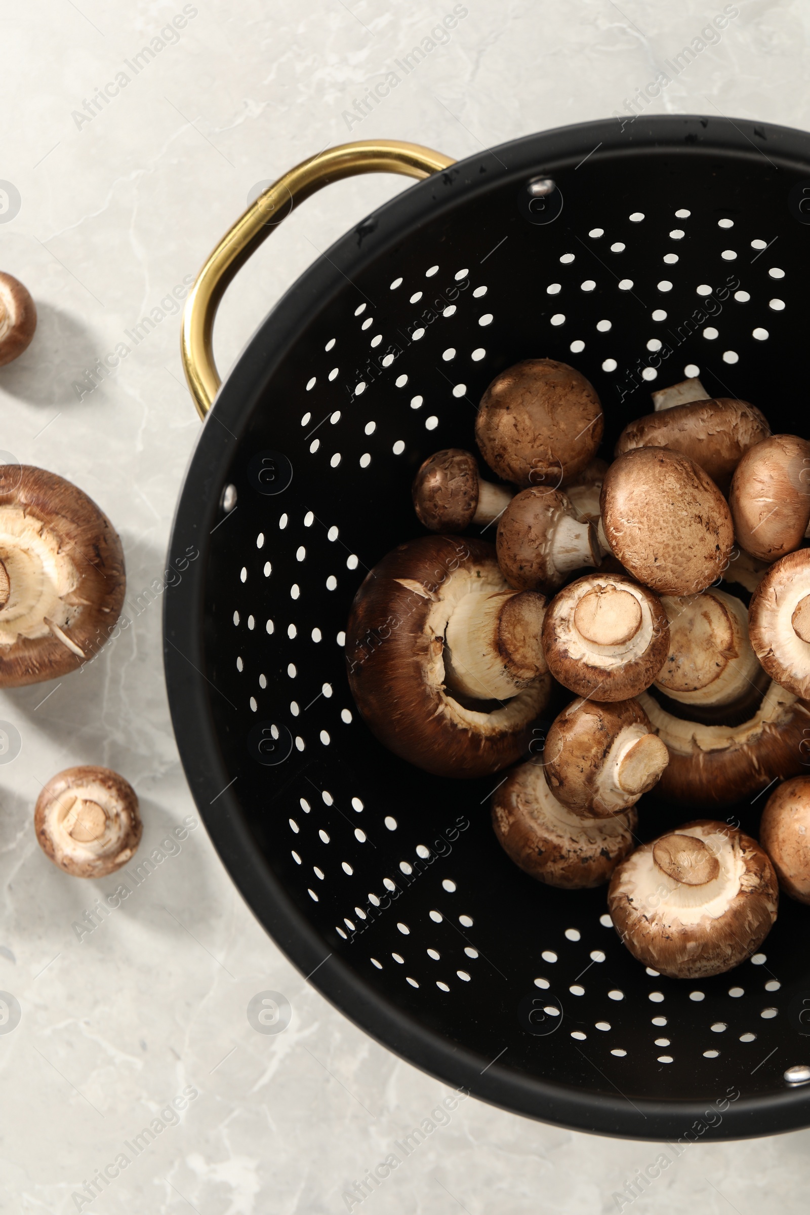 Photo of Raw mushrooms in black colander on marble table, flat lay