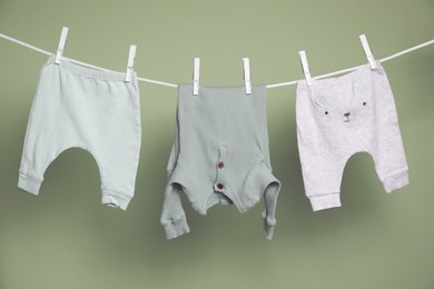 Cute small baby clothes hanging on washing line against green background