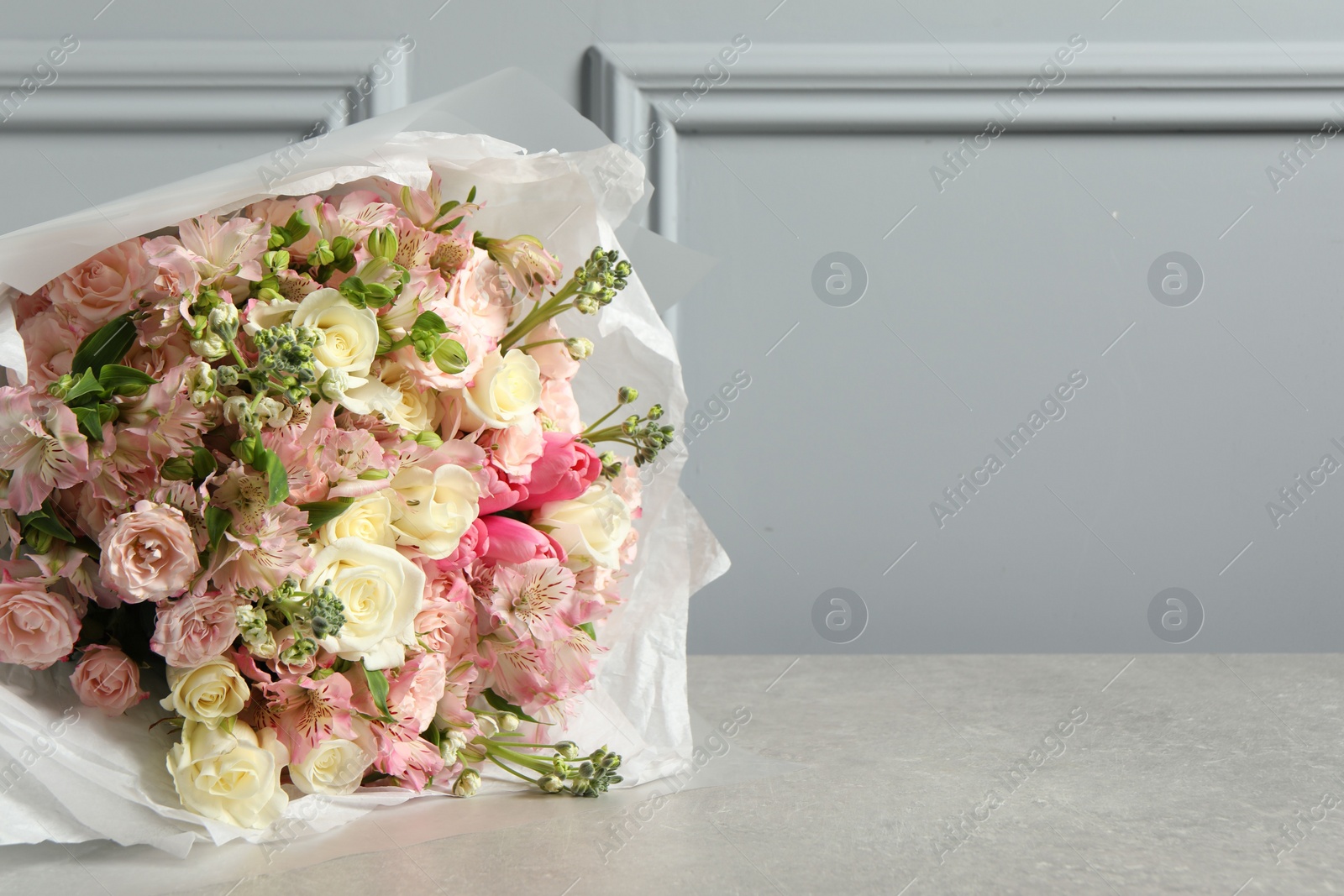 Photo of Beautiful bouquet of fresh flowers on table near grey wall, space for text