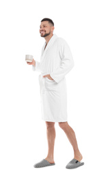 Handsome man in bathrobe with cup of coffee on white background