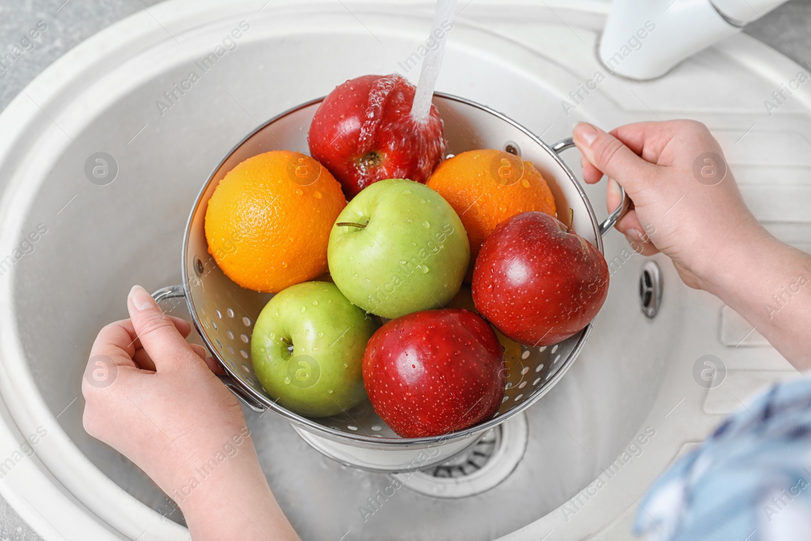 Photo of Woman washing fresh fruits in colander under water, closeup