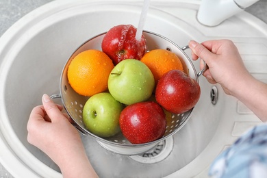 Photo of Woman washing fresh fruits in colander under water, closeup