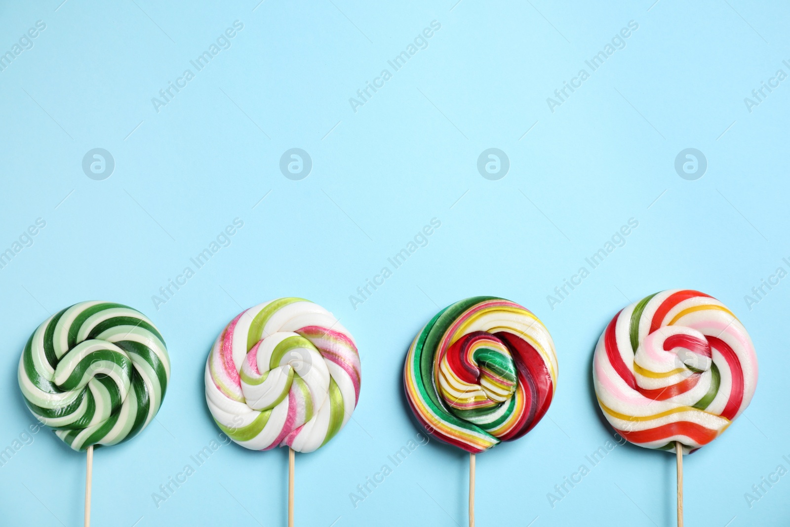 Photo of Sticks with colorful lollipops on light blue background, flat lay. Space for text