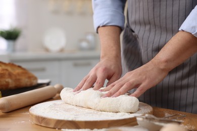 Making bread. Man kneading dough at wooden table in kitchen, closeup