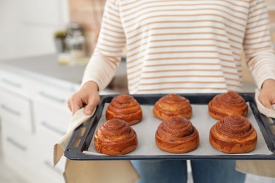Photo of Young woman with tray of oven baked buns in kitchen, closeup