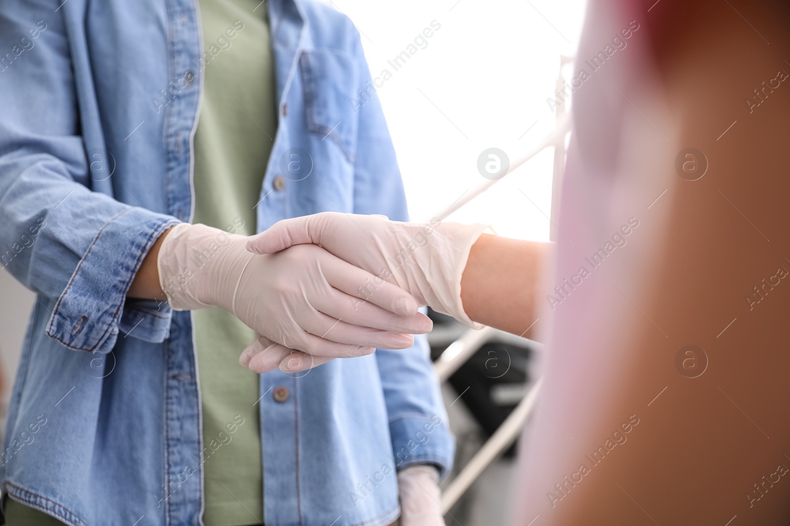 Photo of People in white medical gloves shaking hands on blurred background, closeup