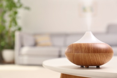 Photo of Modern essential oil diffuser on table in room. Space for text