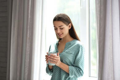 Photo of Young beautiful woman drinking morning coffee near window at home