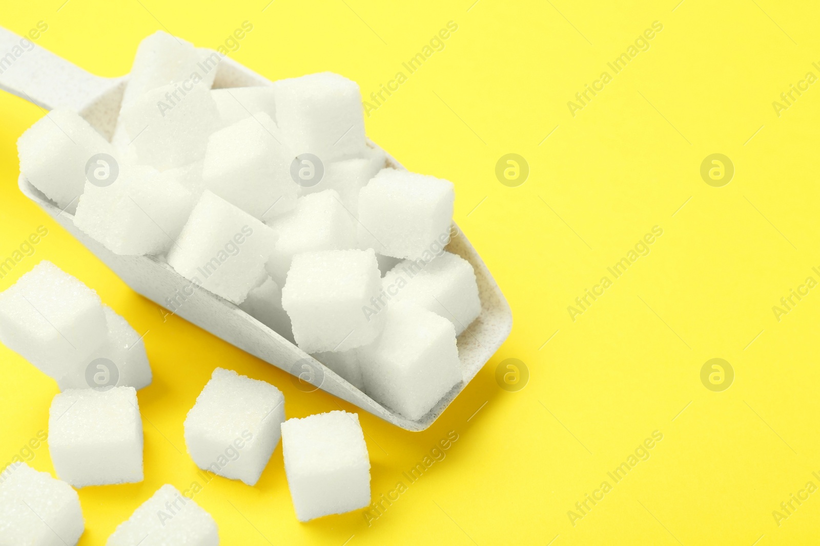 Photo of White sugar cubes and scoop on yellow background