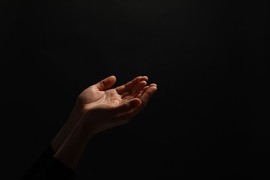 Photo of Religion. Woman with open palms praying on black background, closeup. Space for text