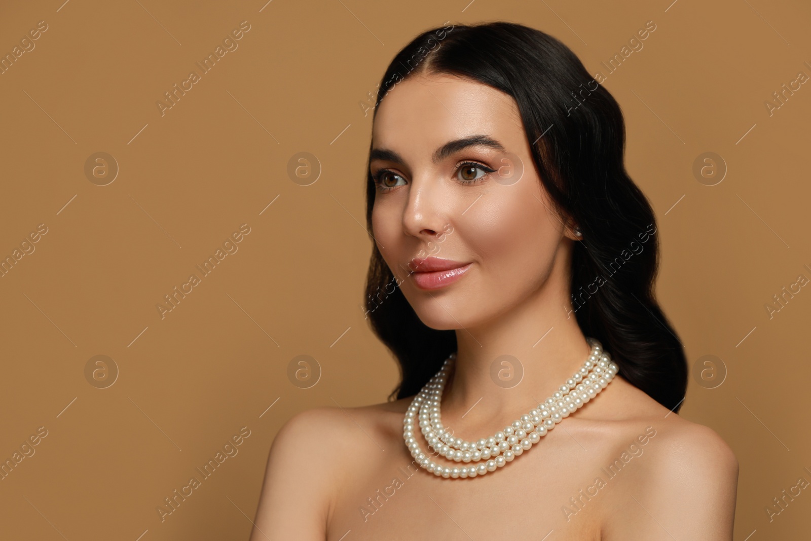 Photo of Young woman wearing elegant pearl jewelry on brown background, space for text