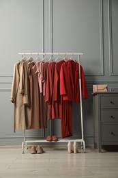 Rack with different stylish women`s clothes, shoes and bag on chest of drawers near grey wall indoors